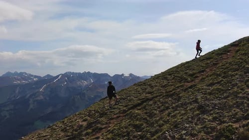 Couple climbing to top of mountain side, aerial side fly view