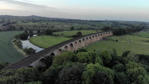 Cinematic aerial drone shot of train viaduct bridge crossing gentle flowing river in yorkshire count