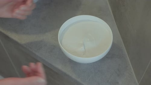 Two hands grab a bowl filled with green clay for a scrub. It takes place in a spa