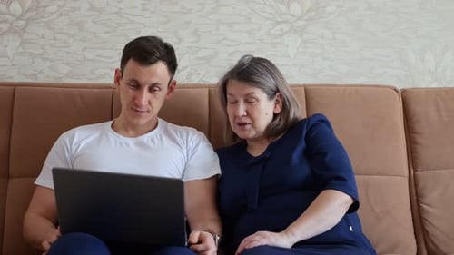 Adult Son Showing Funny Content on Laptop to Elderly Mother