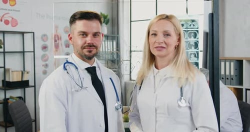 Adult man and woman doctors medics in uniform standing in front of camera in modern hospital workroo