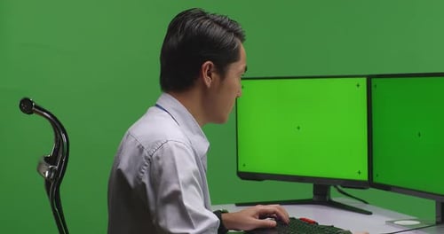 Close Up Of Asian Man Working With Mock Up Multiple Computer Monitor In Green Screen Studio