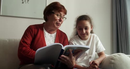 Grandmother Reads to Girl on Sofa at Home