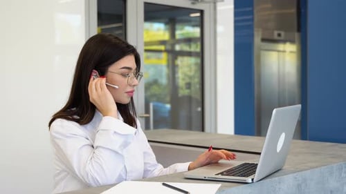Woman Works on Laptop with Headset in Office