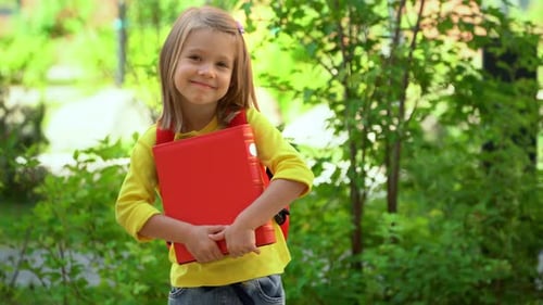 Girl Wih Book Smiles and Laughs in Schoolyard Schoolchild with School Backpack