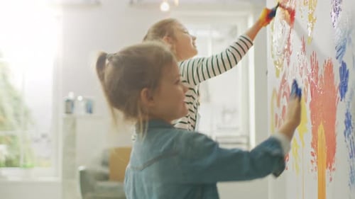 Two Happy Little Girls with Hands Dipped in Colorful Paint Put Handprints and Draw on the Wall. The