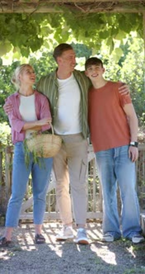 Vertical video: Family holding basket of herbs under arbor, man shifting gaze, expressing affection