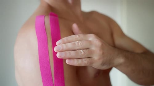 Applying Pink Kinesiology Tape to Shoulder