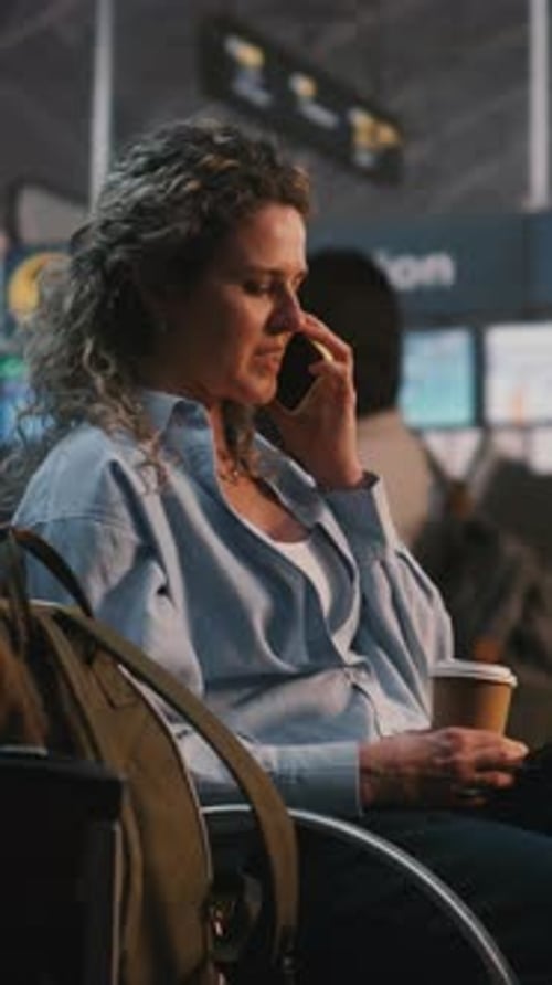 Cheerful Woman Sitting with Luggage and Having Pleasant Mobile Call at Gate