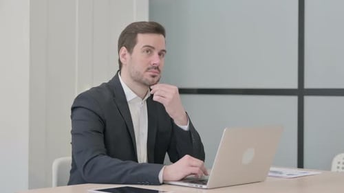 Thoughtful Man Typing on Laptop in Modern Office