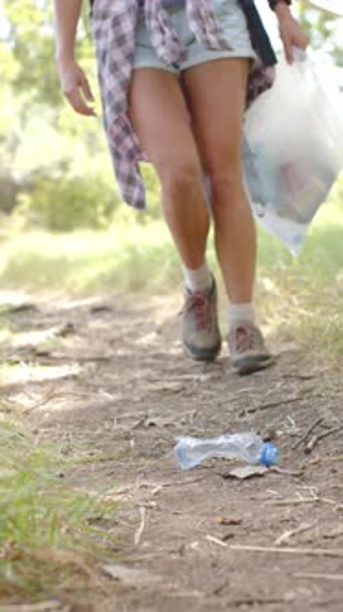 Vídeo vertical: Caminando por un sendero, mujer recogiendo una botella de plástico, promoviendo la conciencia ambiental