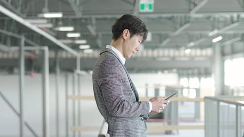 Mature asian realtor works on his smart phone in a vacant warehouse space
