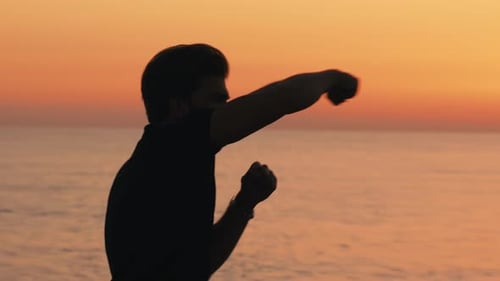 Silhouette of a Boy Boxing at Dawn on the Beach Near the Sea