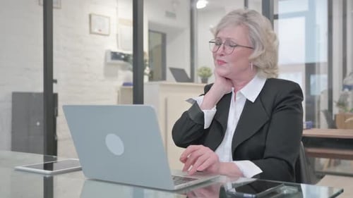 Senior Woman Working at Laptop Massaging Stiff Neck