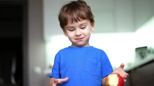 Beautiful smiling baby boy eating an apple. Kid drops the fruit and stands looking at it.