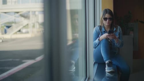 Woman with sunglasses sitting next to big window at the terminal gate