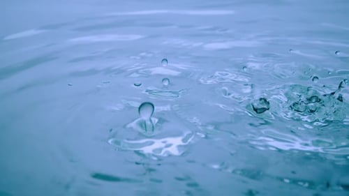 Drops of Water Falling on a Blue Liquid Surface and Forming Waves and Splashes