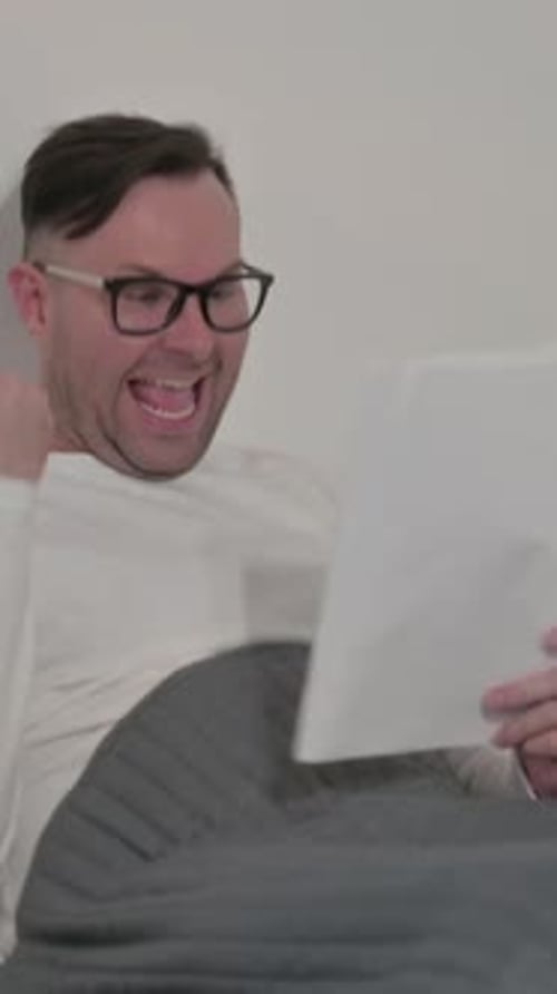 Excited Man Reading Documents While in Bed