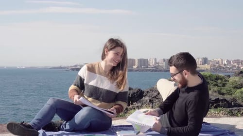 Students sitting learning and studying for exams near the sea