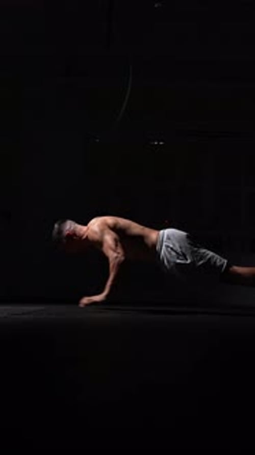 Un homme musclé fait preuve d'une force extrême en effectuant des tractions dans une salle de sport sombre