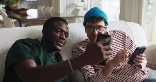 Two Young Men Using Smartphones on Sofa Indoors