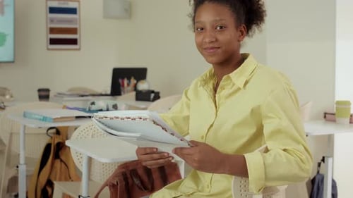 Young Woman Smiling in Classroom Holding Notebooks