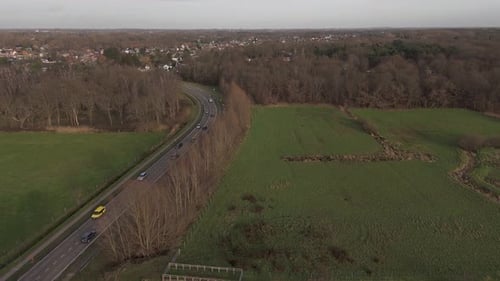Drone shot of cars on a road passing through grass lands and nature on a province road during a sunn