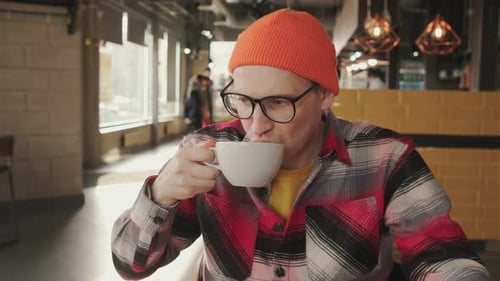 A Man with Glasses and a Orange Hat Enjoying a Cup of Coffee Sitting in a Coffee Shop