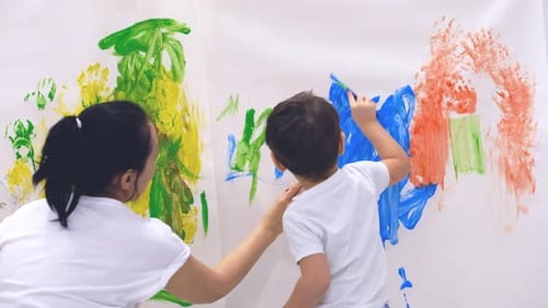 Close Up of Happy Little Child Making Colorful Handsprint on the White Wall with Mother Together