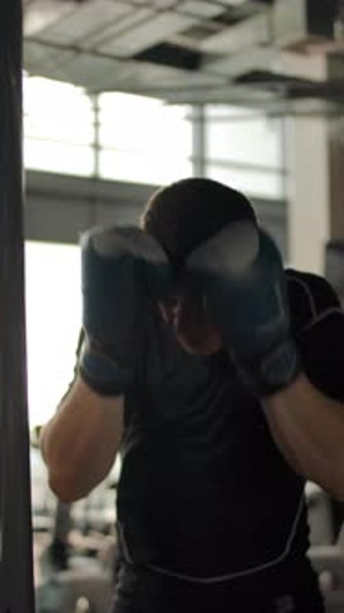 Vertical of Closeup of an Aggressive Caucasian Man Hitting a Punching Bag in a Gym