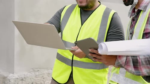 Male supervisor explains construction plan on laptop, tablet to junior engineer. Asian workers in ye
