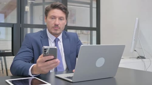 Man Working on Laptop and Using Phone in Office