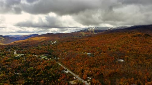 Grey dramatic clouds move by the sky above the colorful forests. Stunning autumn scenery of Vermont
