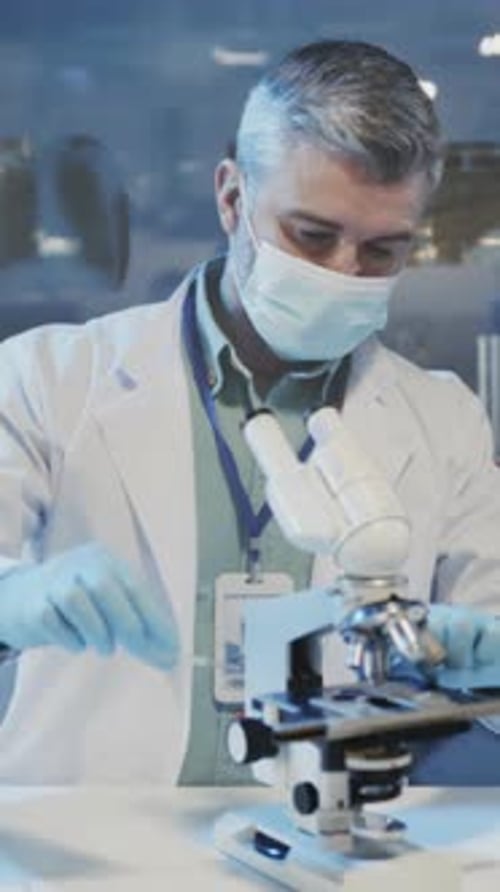 Man Using Microscope in Laboratory Wearing Mask Gloves