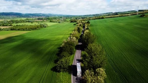 Aerial landscape shot of cloudy bright and shady view of agricultural areas hills following road veh