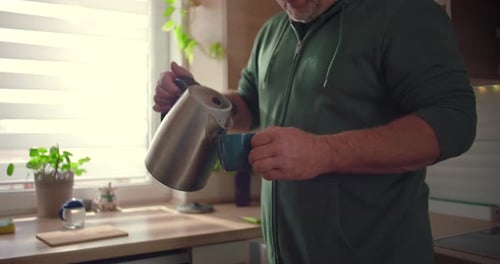 Close-up of hands pouring hot water into mug, kitchen activity, morning routine, making tea or