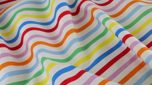 Top view of the soft folds of white cotton fabric with rainbow stripes rotated on the display case.