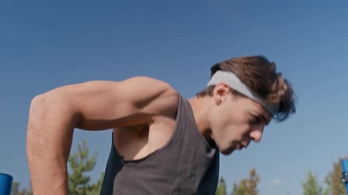 Junger starker Mann macht Tauchgänge auf Parallelstangen auf einem Sportplatz im Freien