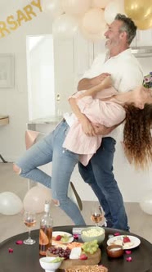 Vertical video: Senior couple marking anniversary dancing under RSARY banner with balloons at home