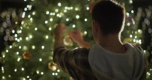 Person Decorating Christmas Tree with Golden Ornaments
