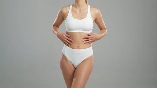 Jeune femme blonde en forme et belle en maillot de bain blanc posant sur fond gris Healthcare Diet