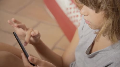 A cute little girl sitting on the floor and touching her smartphone, looking interested. Close-up sh