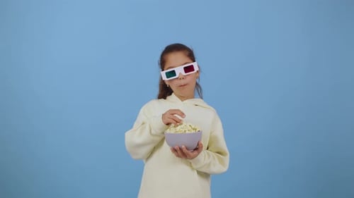Child Enjoys Popcorn While Wearing Colorful 3D Glasses in a Bright Blue Setting Creating a Fun and