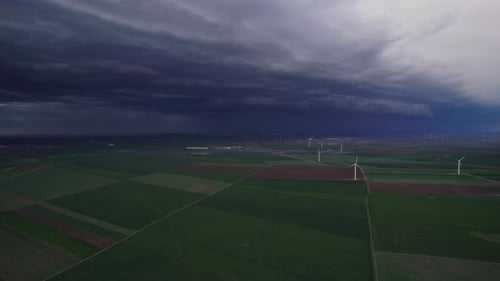 Wind turbines on a green landscape with a dramatic stormy sky overhead