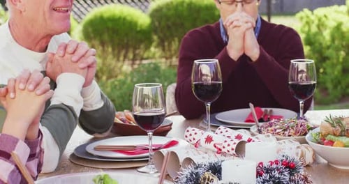 Happy caucasian family praying before dinner in garden