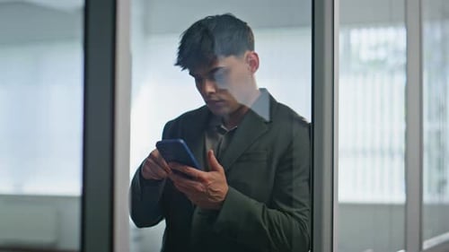 Fokussierter Manager liest Smartphone-Nachricht in der Nähe einer Glaswand, Büro, Nahaufnahme