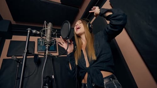 girl singer singing in a recording studio with headphones in front of microphone to create a song