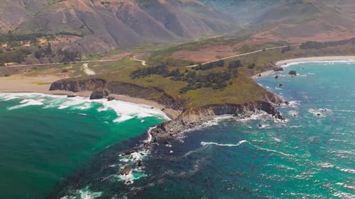 Craggy shore of the Pacific Ocean at Morro Bay, California, USA. Bare brown mountains at backdrop.
