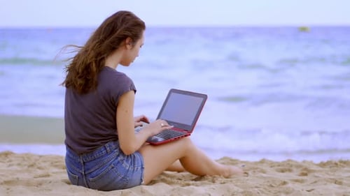 Brünette Frau arbeitet im Urlaub aus der Ferne mit Laptop am Meer