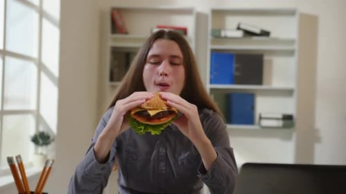 Frau isst Burger im Büro. Ein junger Angestellter isst mittags Cheeseburger
.